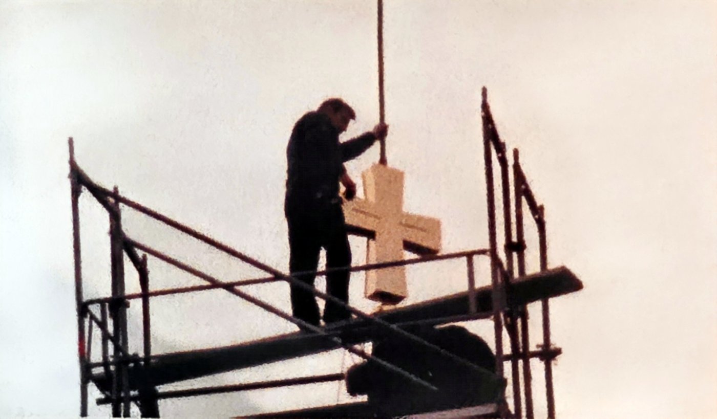 Ein Arbeiter auf dem Gerüst an der Turmspitze setzt das neue Kreuz auf